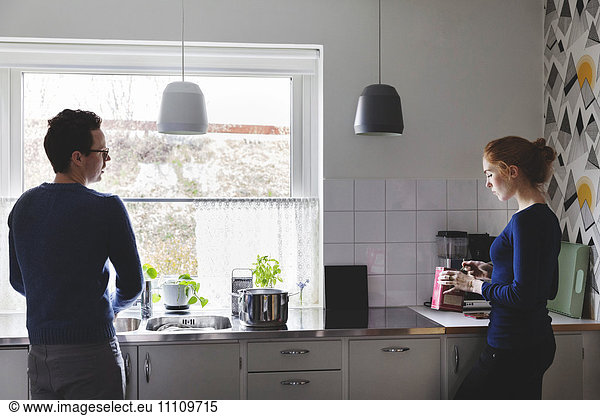 Mann wäscht Geschirr  während Frau in der Küche kocht.