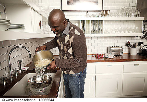 Mann wäscht zu Hause Spaghetti in Geschirr