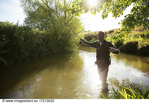 Mann wirft Fliegenfischerrute an sonnigen idyllischen Fluss
