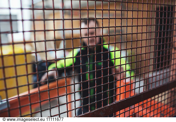 Manual worker in reflective clothing seen through metal grate