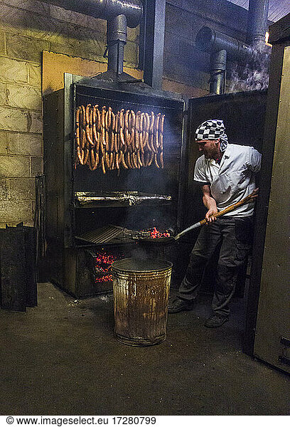Manual worker inserting coal in smokehouse while preparing sausages at food factory