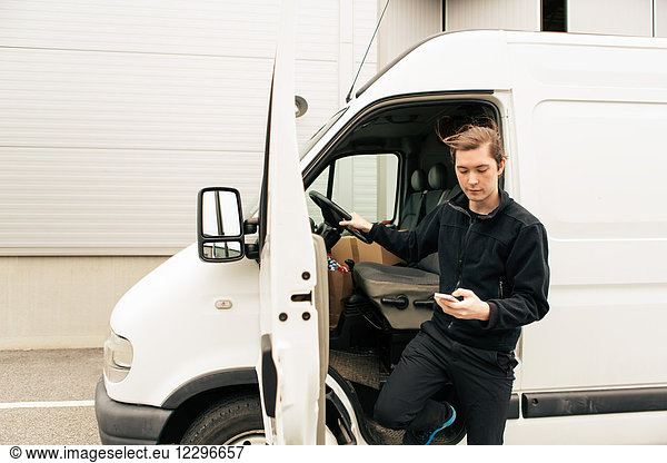 Manual worker using mobile phone while standing by delivery van