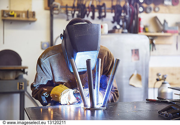 Manual worker welding metallic stool at wood shop