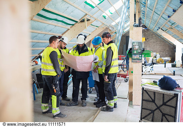 Manual workers with manager reading blue prints at construction site