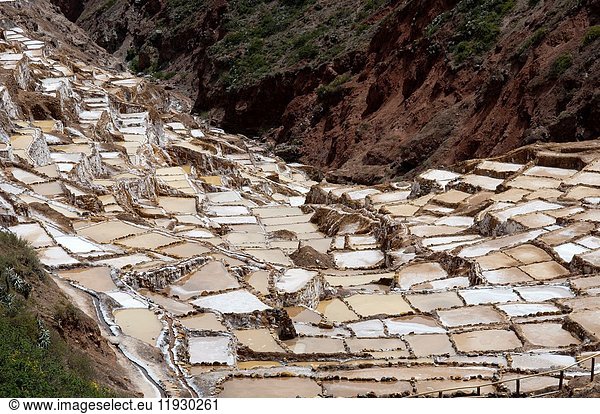 Maras's saltworks in the Sacred Valley near Cuzco. Maras is a town in the Sacred Valley of the Incas  40 kilometers north of Cuzco  in the Cuzco Region of Peru. The town is well known for its nearby salt evaporation ponds  in use since Inca times. The salt-evaporation ponds are up-slope  less than a kilometer west of the town. The Maras area is accessible only by a poorly maintained dirt road  which leads from the main road leading through the Sacred Valley between Cuzco and the surrounding towns. Tourist sites in the area include the colonial church  the local salt evaporation ponds  and the surrounding scenery. Since pre-Inca times  salt has been obtained in Maras by evaporating salty water from a local subterranean stream. The highly salty water emerges at a spring  a natural outlet of the underground stream. The flow is directed into an intricate system of tiny channels constructed so that the water runs gradually down onto the several hundred ancient terraced ponds. Almost all the ponds are less than four meters square in area  and none exceeds thirty centimeters in depth. All are necessarily shaped into polygons with the flow of water carefully controlled and monitored by the workers. The altitude of the ponds slowly decreases  so that the water may flow through the myriad branches of the water-supply channels and be introduced slowly through a notch in one sidewall of each pond. The proper maintenance of the adjacent feeder channel  the side walls and the water-entry notch  the pond's bottom surface  the quantity of water  and the removal of accumulated salt deposits requires close cooperation among the community of users. It is agreed among local residents and pond workers that the cooperative system was established during the time of the Incas  if not earlier. As water evaporates from the sun-warmed ponds  the water becomes supersaturated and salt precipitates as various size crystals onto the inner surfaces of a pond's earthen walls and on the pond's earthen floor. The pond's keeper then closes the water-feeder notch and allows the pond to go dry. Within a few days the keeper carefully scrapes the dry salt from the sides and bottom  puts it into a suitable vessel  reopens the water-supply notch  and carries away the salt. Color of the salt varies from white to a light reddish or brownish tan  depending on the skill of an individual worker. Some salt is sold at a gift store nearby.