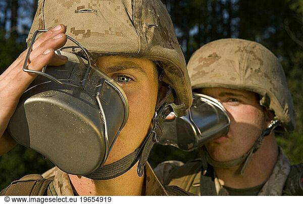 Marine recruits drink soup from canteens during a field training exercise. Each marine is wearing desert camouflage uniform and helmets.
