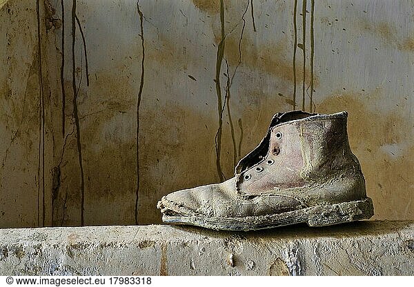 Maroder Arbeitsstiefel aus Leder steht auf Mauer  verrotteter Schuh  Schuhwrack  vergammelter Treter  ausgelatschter Schuh  abgetragener Schuh  alter Schuh