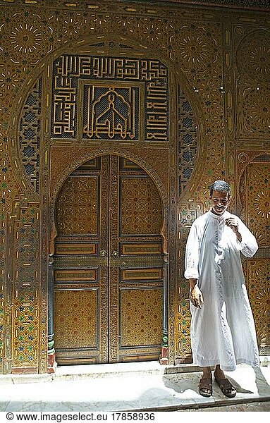 Marokkanischer Mann im Djelabba oder marokkanischen Kapuzenmantel  hinten das Tor des Sarkophargs von Mouloay Idris  Altstadt  Fes  Marokko  Afrika