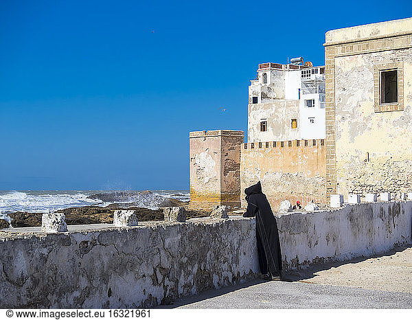Marokko  Essaouira  Berber in schwarzer Djellaba an der Hafenmauer