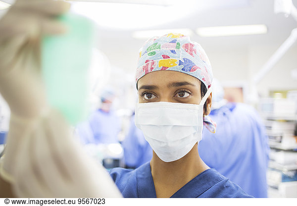 Masked surgeon adjusting saline bag during surgery