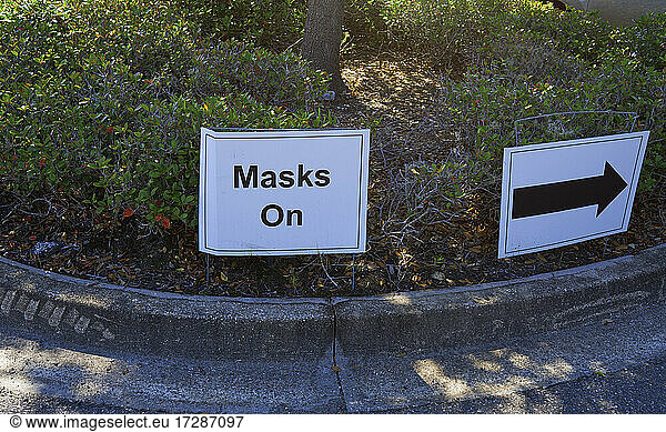 Masks On sign with directional arrow symbol on hedge