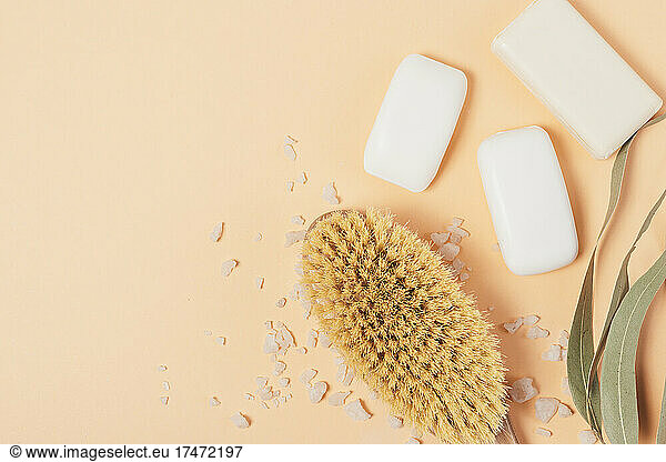Massage brush with soap bars and bath salt on peach background