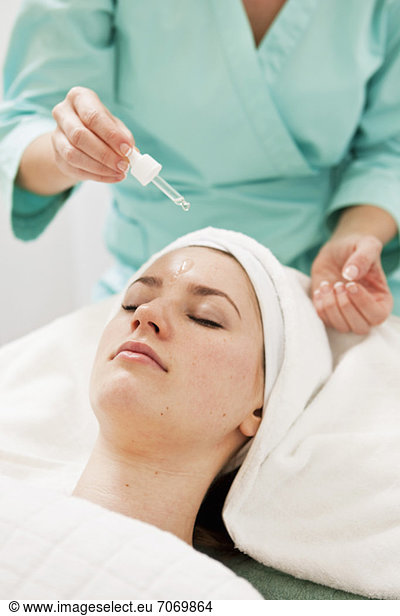 Massage therapist applying oil from pipette on young woman's forehead