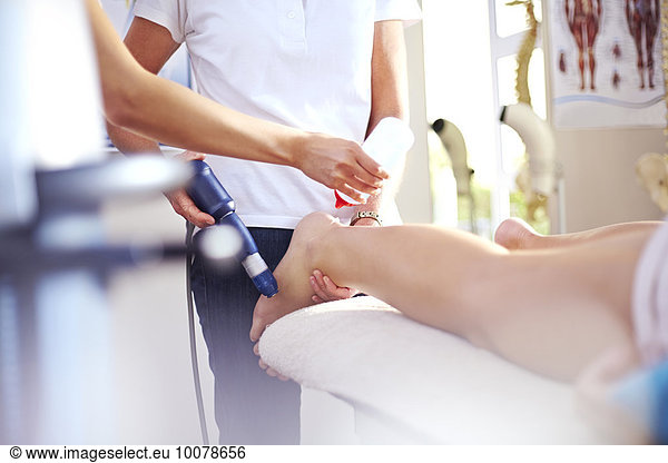 Masseuse applying gel to woman’s leg in preparation for ultrasound probe