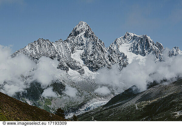 Massive peaks in french alps surrounded by clouds with glaciers below