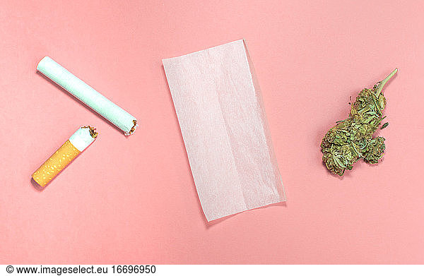 Materialien zum Drehen eines Cannabis-Joints mit Tabak auf rosa Hintergrund.