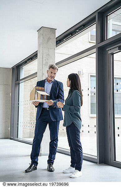 Mature architect discussing with colleague over model house in office
