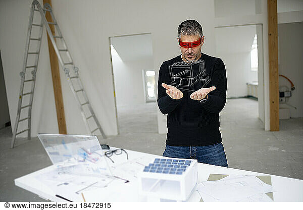 Mature architect wearing virtual reality simulator looking at house model
