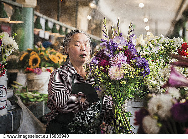Mature Asian woman arranges flowers at Pike Place Market in Seattle