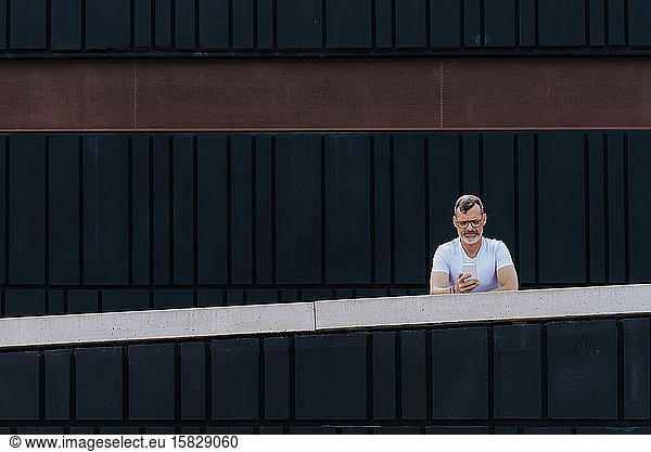 Mature bearded man using a mobile phone leaning on a fence