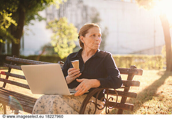 Mature business woman eating ice cream using laptop computer in park