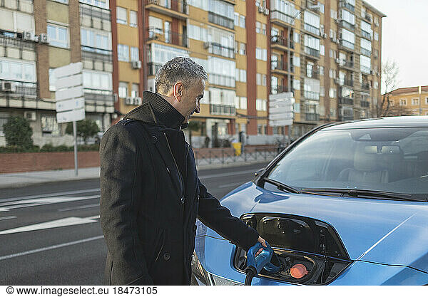 Mature businessman charging electric car at station