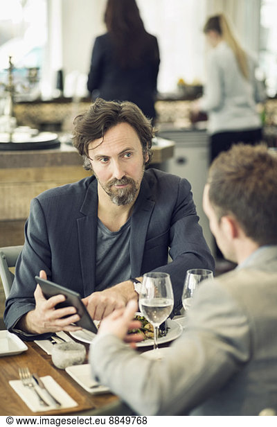 Mature businessman discussing over digital tablet with colleague at restaurant table