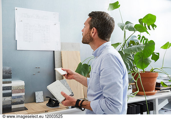 Mature businessman examining blueprints hanging on bulletin board at creative office