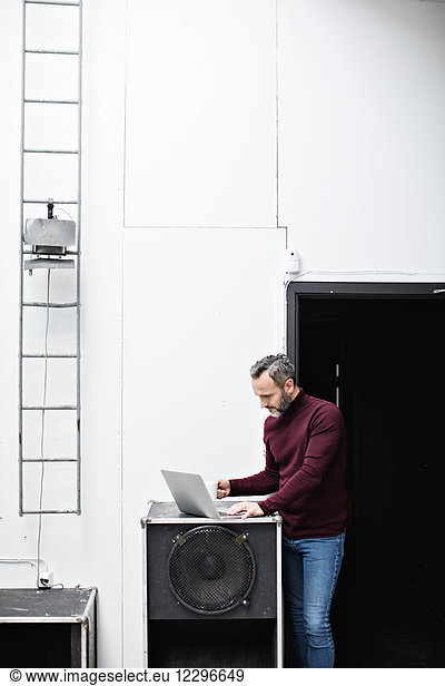 Mature businessman having coffee and using laptop while standing by wall at creative office
