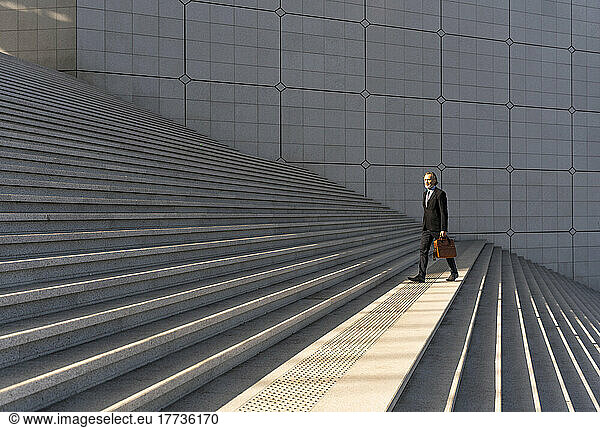 Mature businessman holding bag walking on staircase