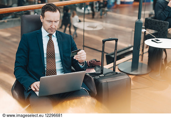Mature businessman holding credit card while using laptop in airport
