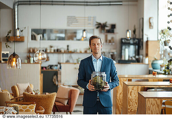 Mature businessman holding glass container standing at cafe