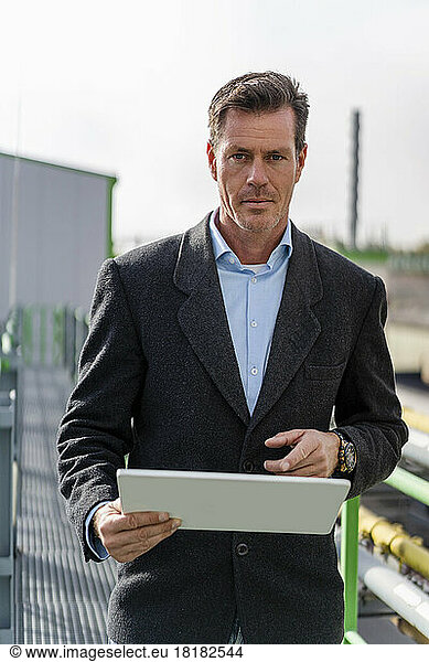 Mature businessman holding tablet PC standing at industrial plant