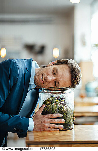 Mature businessman leaning on glass container with plant at coffee shop