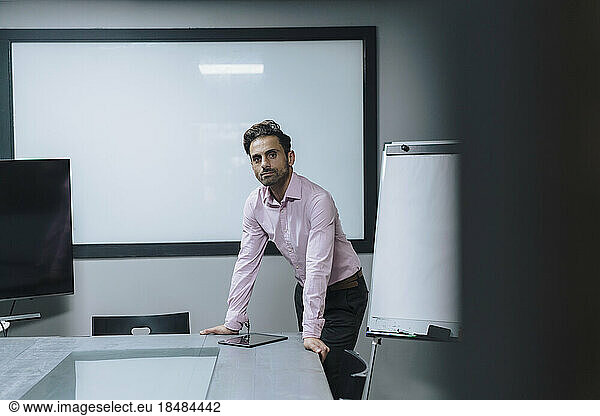 Mature businessman leaning on table in meeting room at office