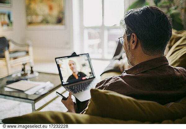 Mature businessman on video call with male colleague in living room during pandemic