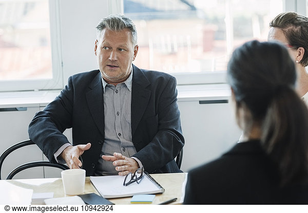 Mature businessman sitting and explaining coworkers at office