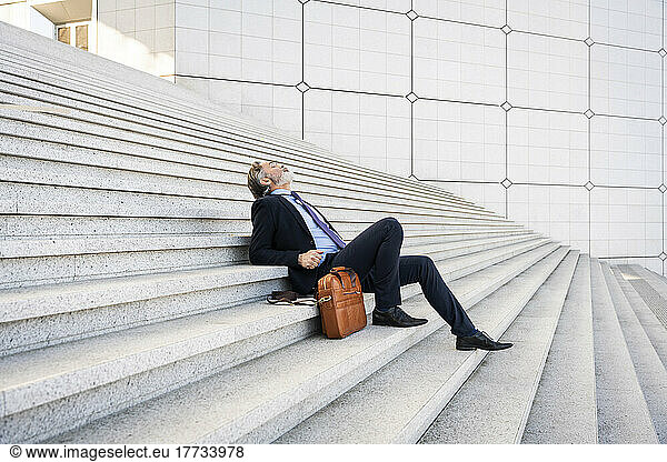 Mature businessman sitting by bag relaxing on steps