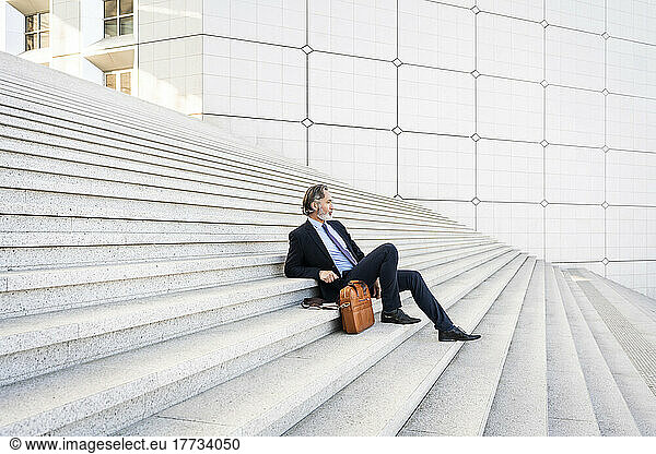 Mature businessman sitting with bag on steps
