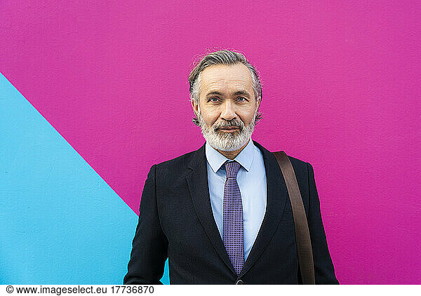 Mature businessman standing in front of pink and blue wall