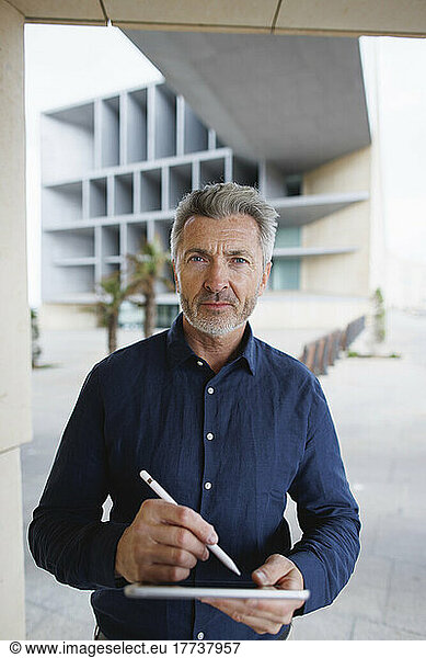 Mature businessman standing with tablet PC and digitized pen