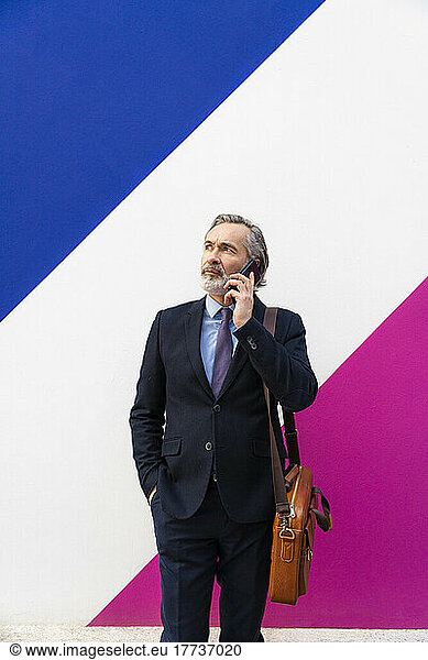 Mature businessman talking on mobile phone in front of multi colored wall