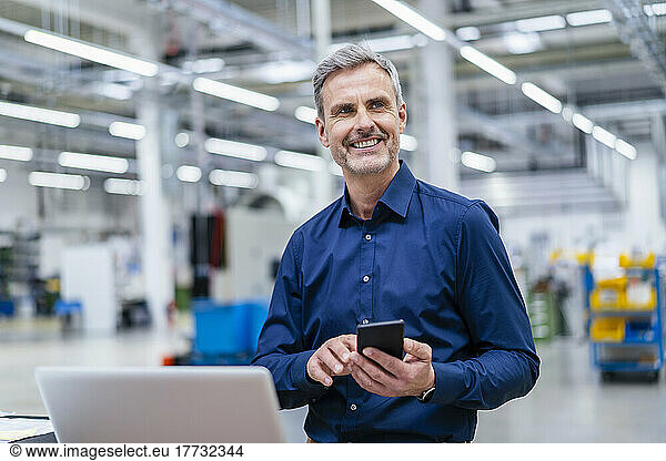 Mature businessman using laptop and smartphone in factory