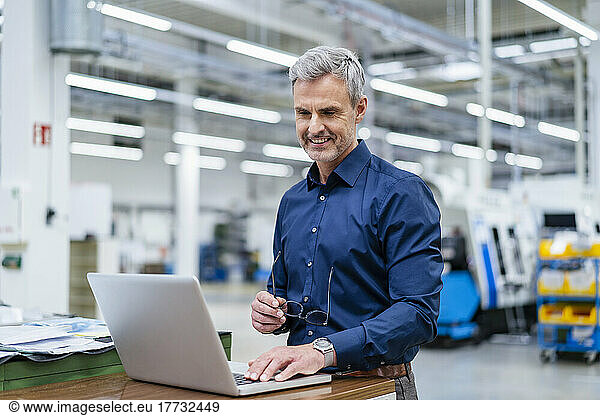 Mature businessman using laptop in factory