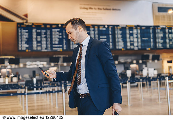 Mature businessman using mobile phone while walking in airport terminal