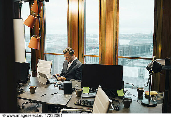 Mature businessman using smart phone at table in board room