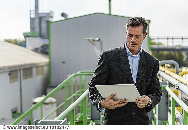 Mature businessman using tablet PC standing at industrial plant