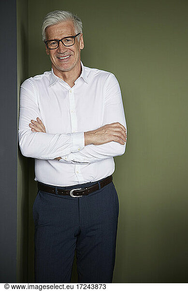 Mature businessman with arms crossed leaning on wall