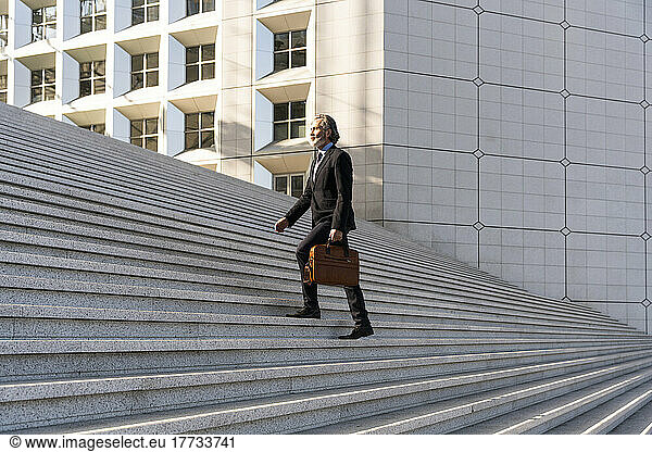 Mature businessman with bag moving up on staircase
