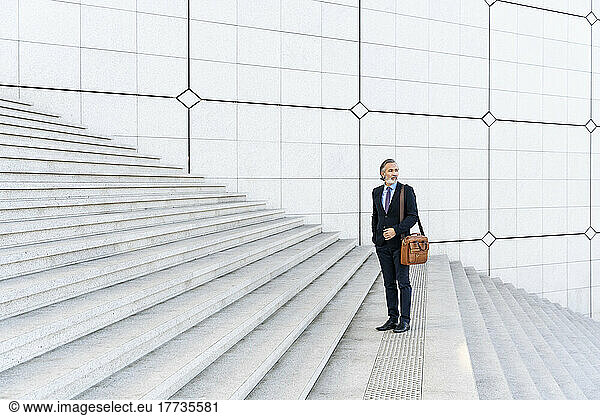Mature businessman with bag standing on staircase